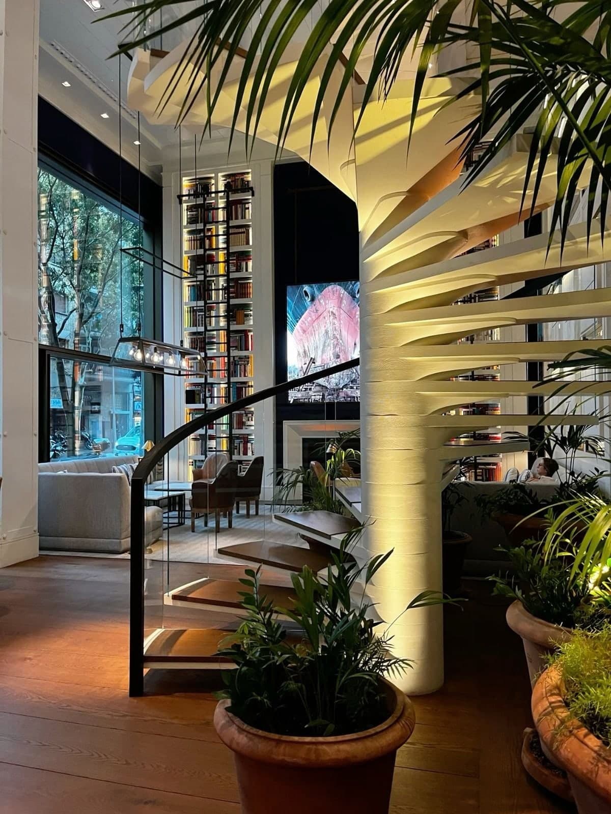 A hotel lobby with a sculptural spiral staircase, plants and floor-to-ceiling windows