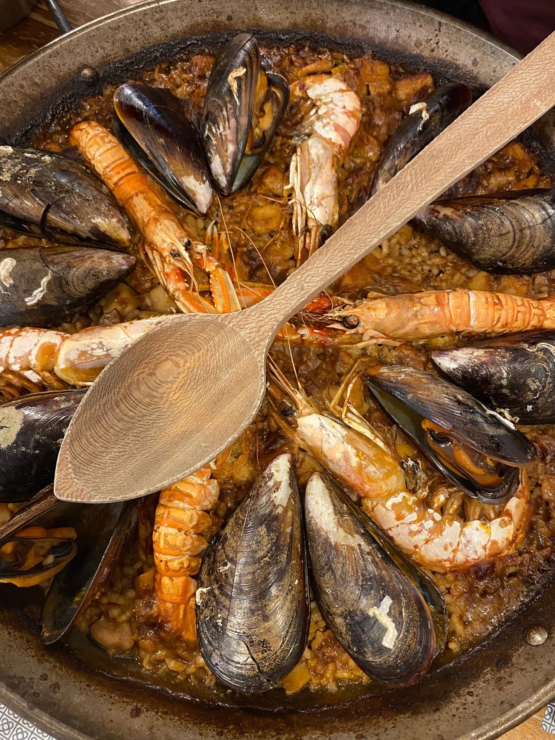 Seafood paella with mussels and prawns, a wooden spoon resting in the pan