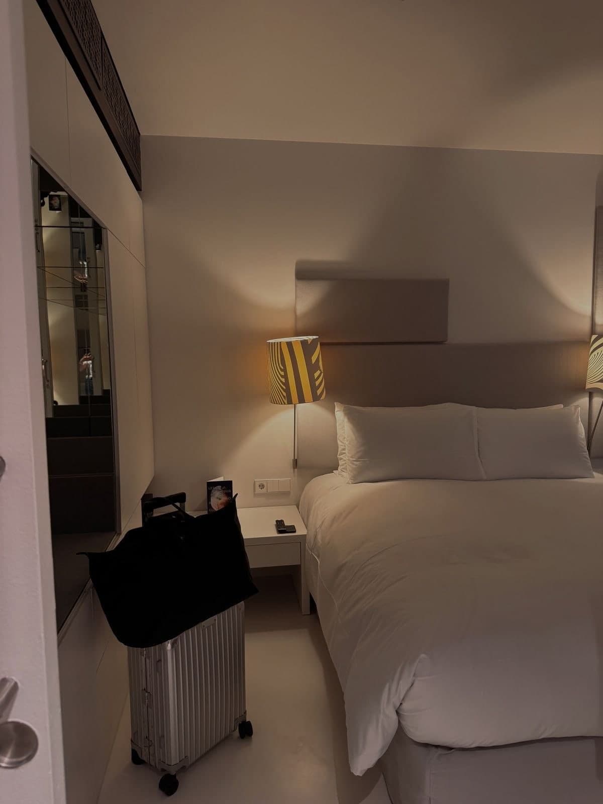 A hotel room in the evening, bedside lamp on, a suitcase by the bed