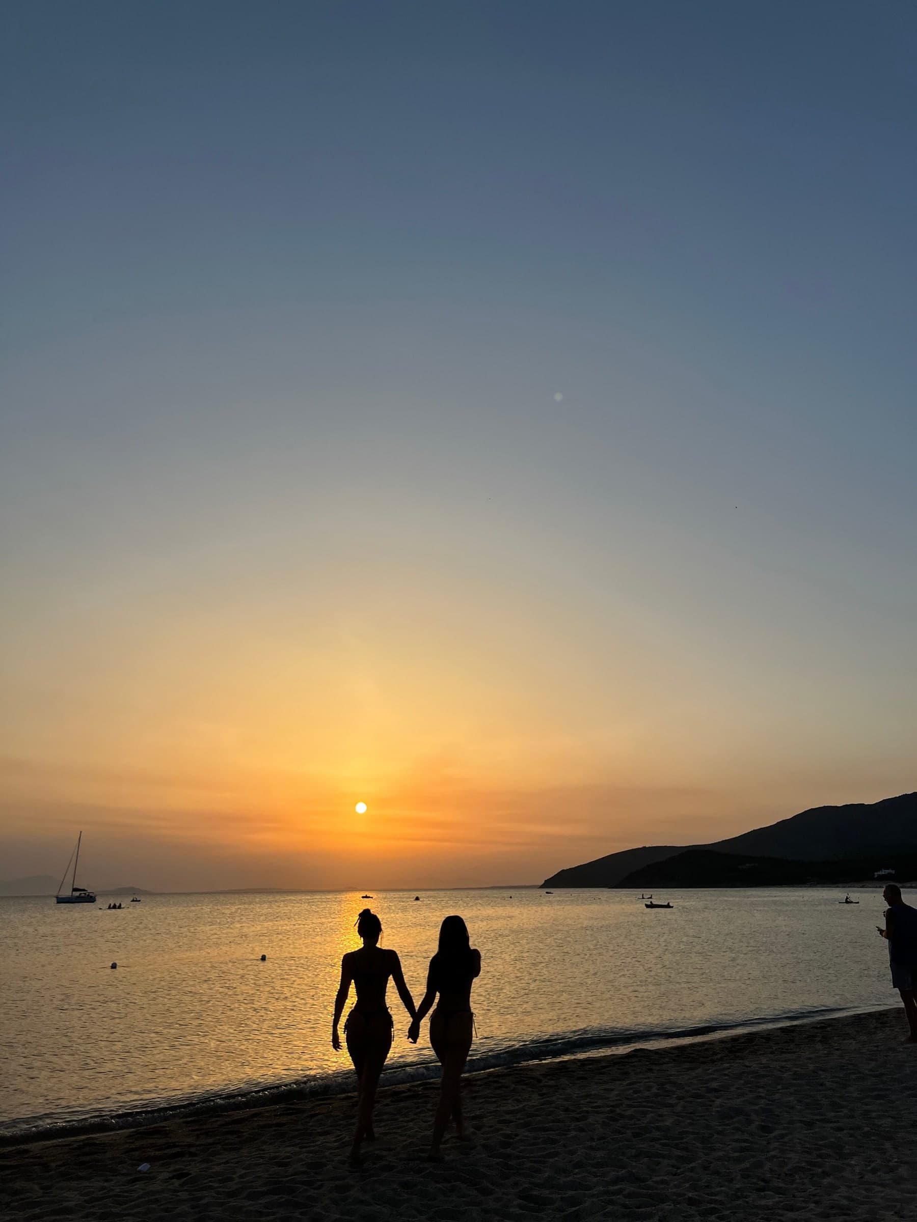 Two people walking on the beach at sunset, silhouetted against the sun