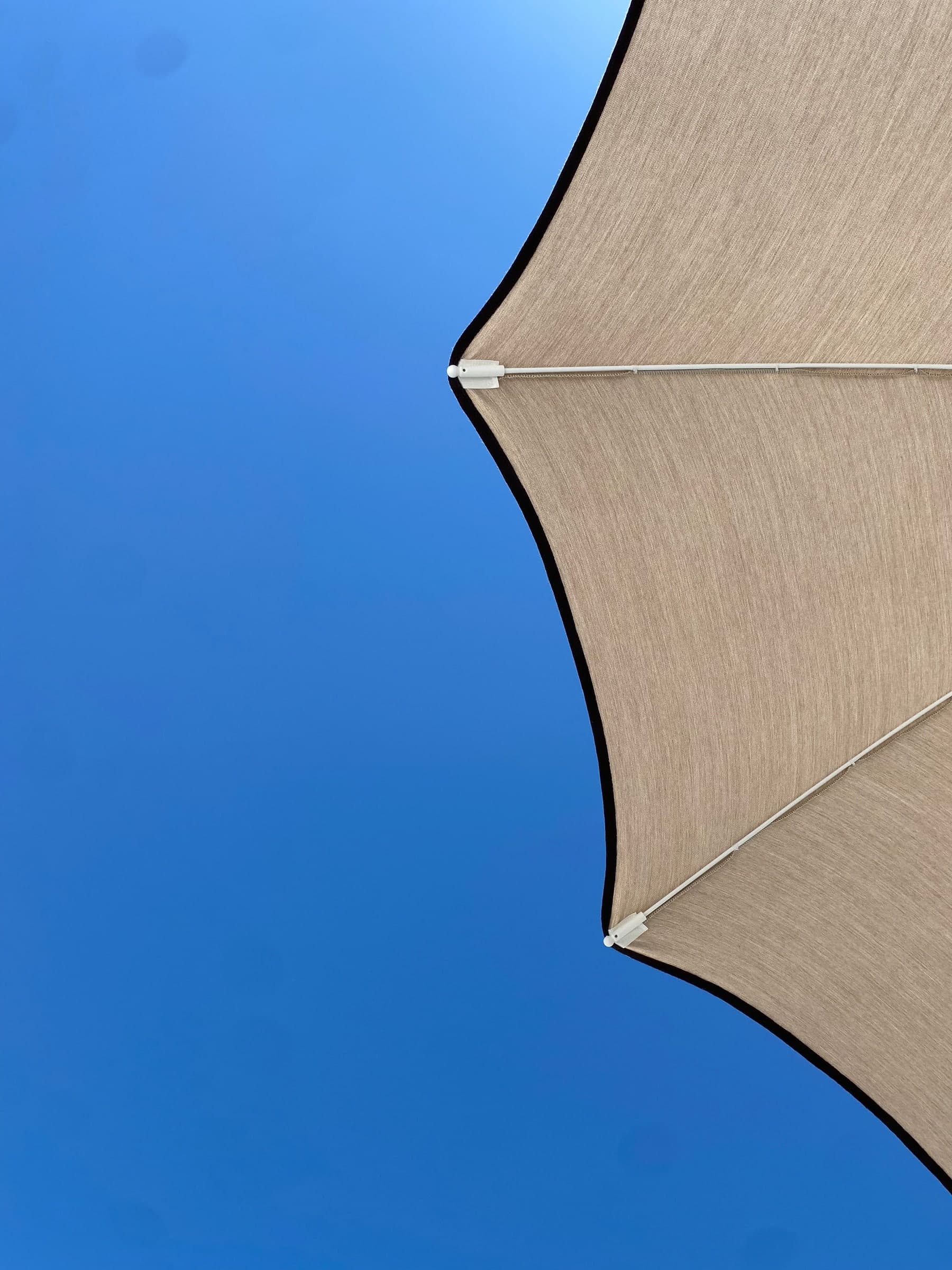 The edge of a beige beach umbrella against a deep blue sky
