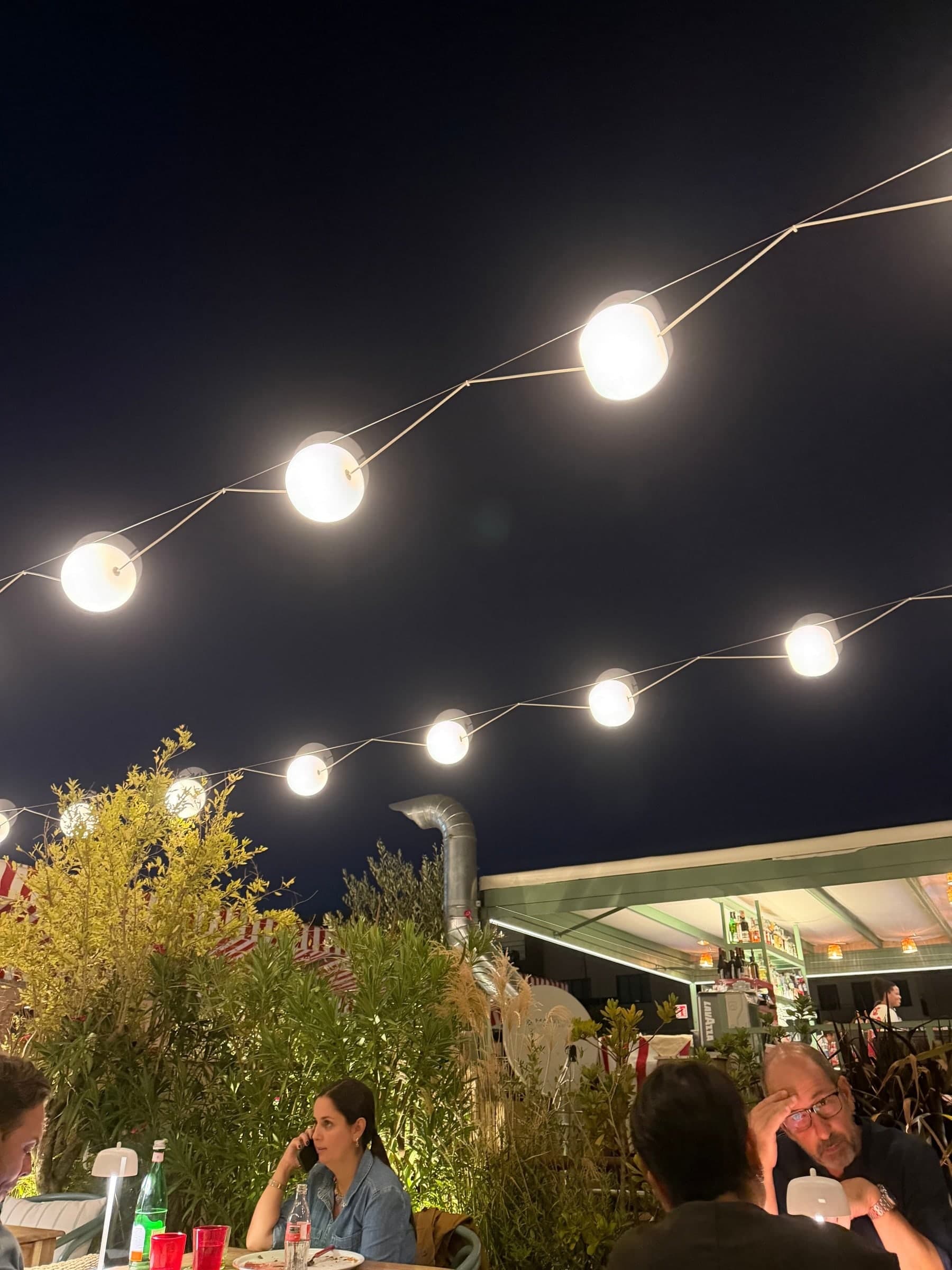 The rooftop terrace after dark, string lights overhead and guests at the tables