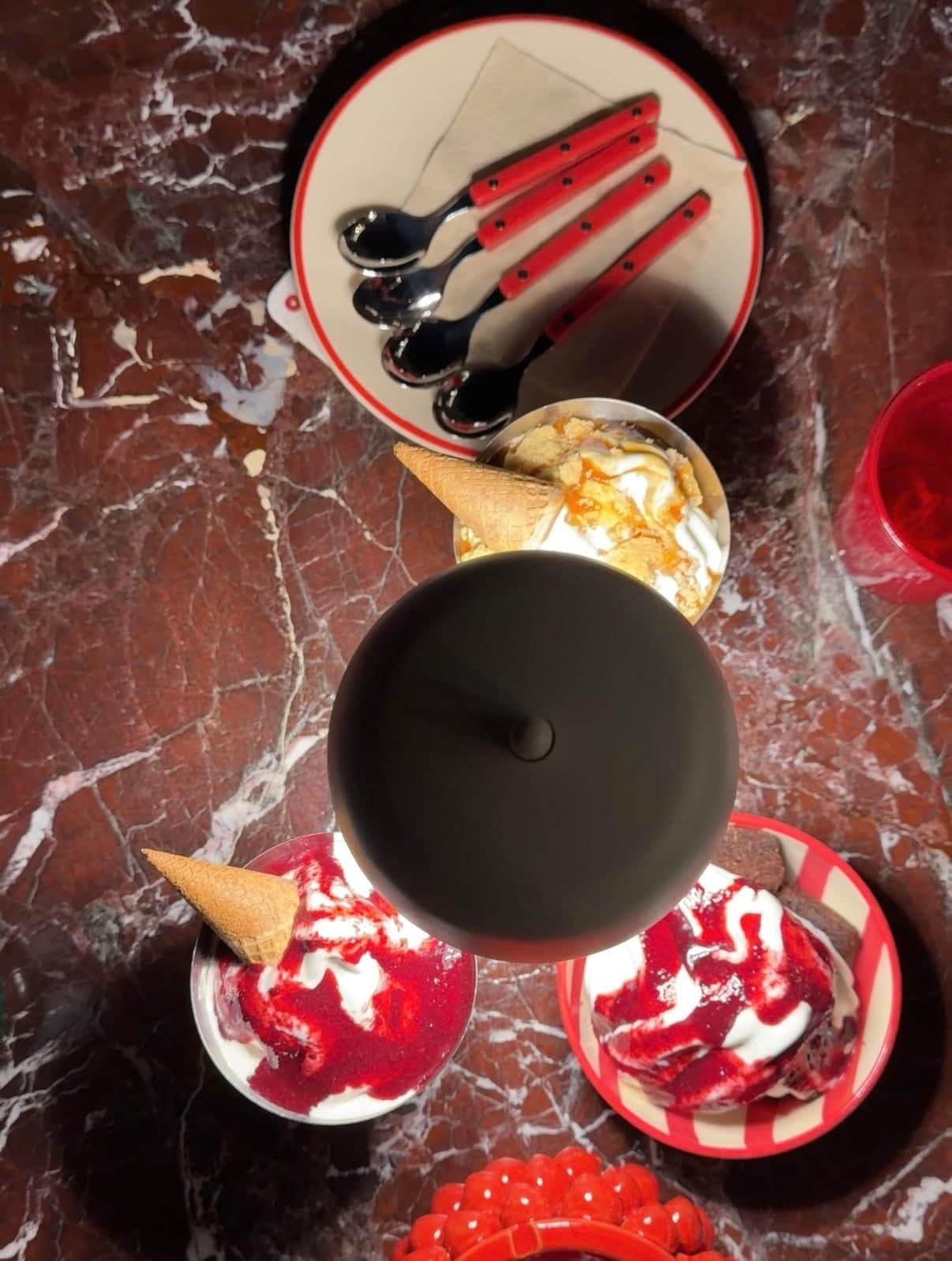 Gelato cups and cones with red sauce on a red marble table, from above