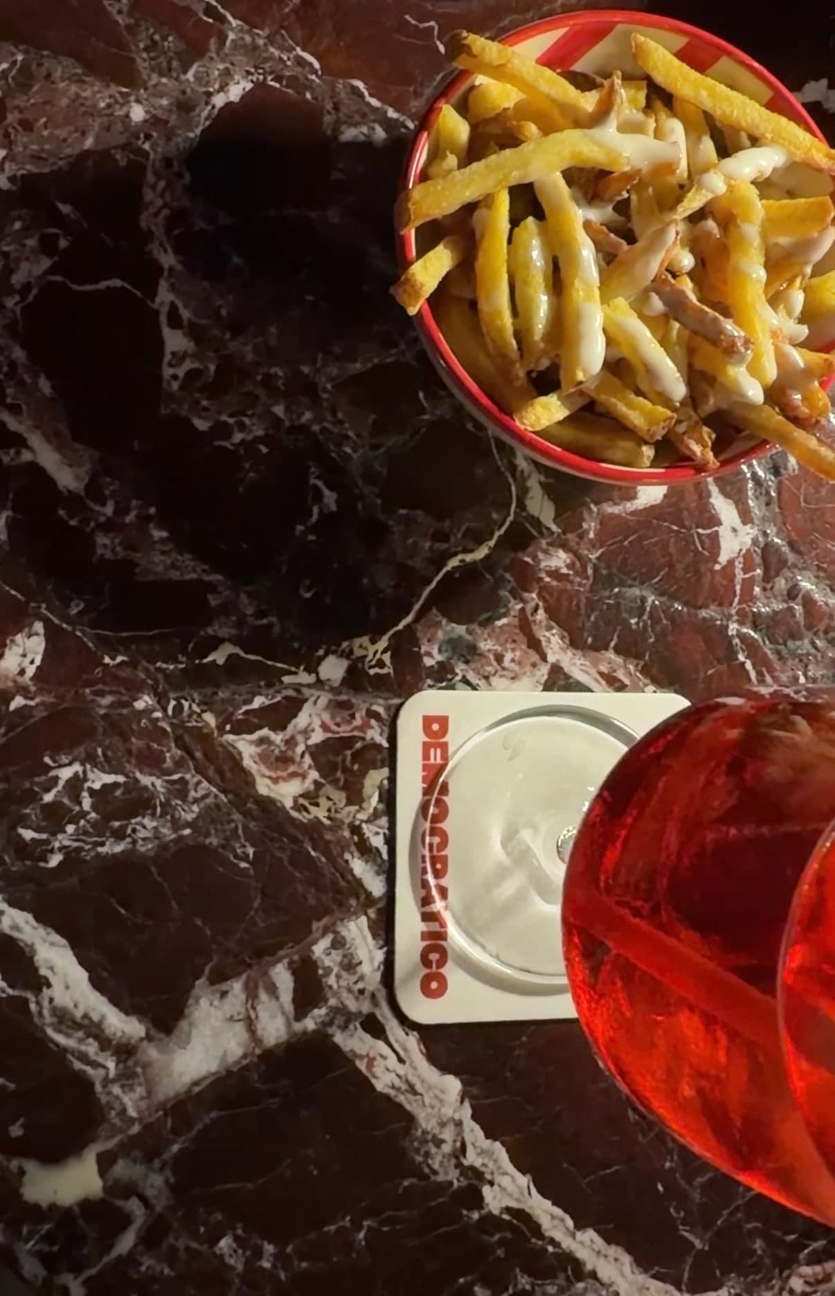 Fries and a spritz on red marble, a Democratico coaster under the glass