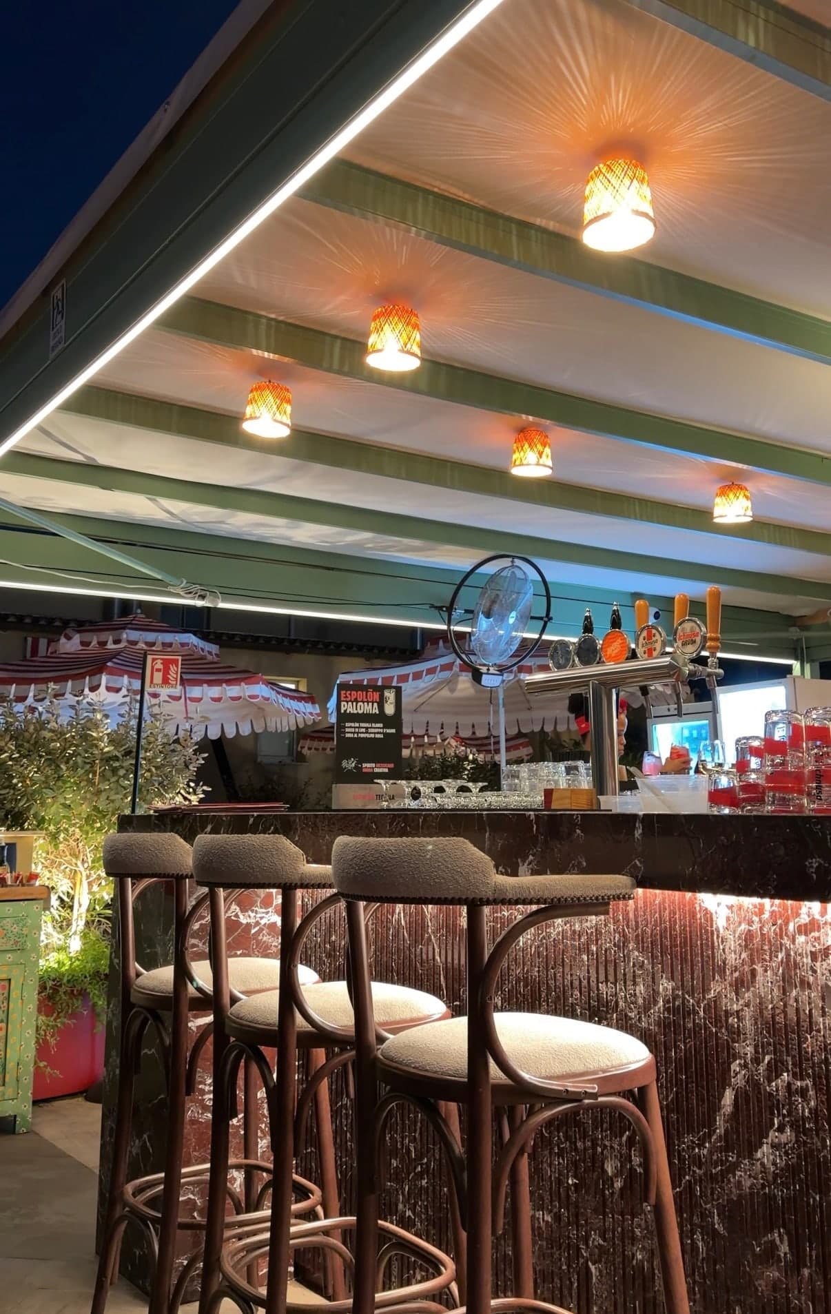 The bar under a pergola with warm pendant lights and upholstered stools