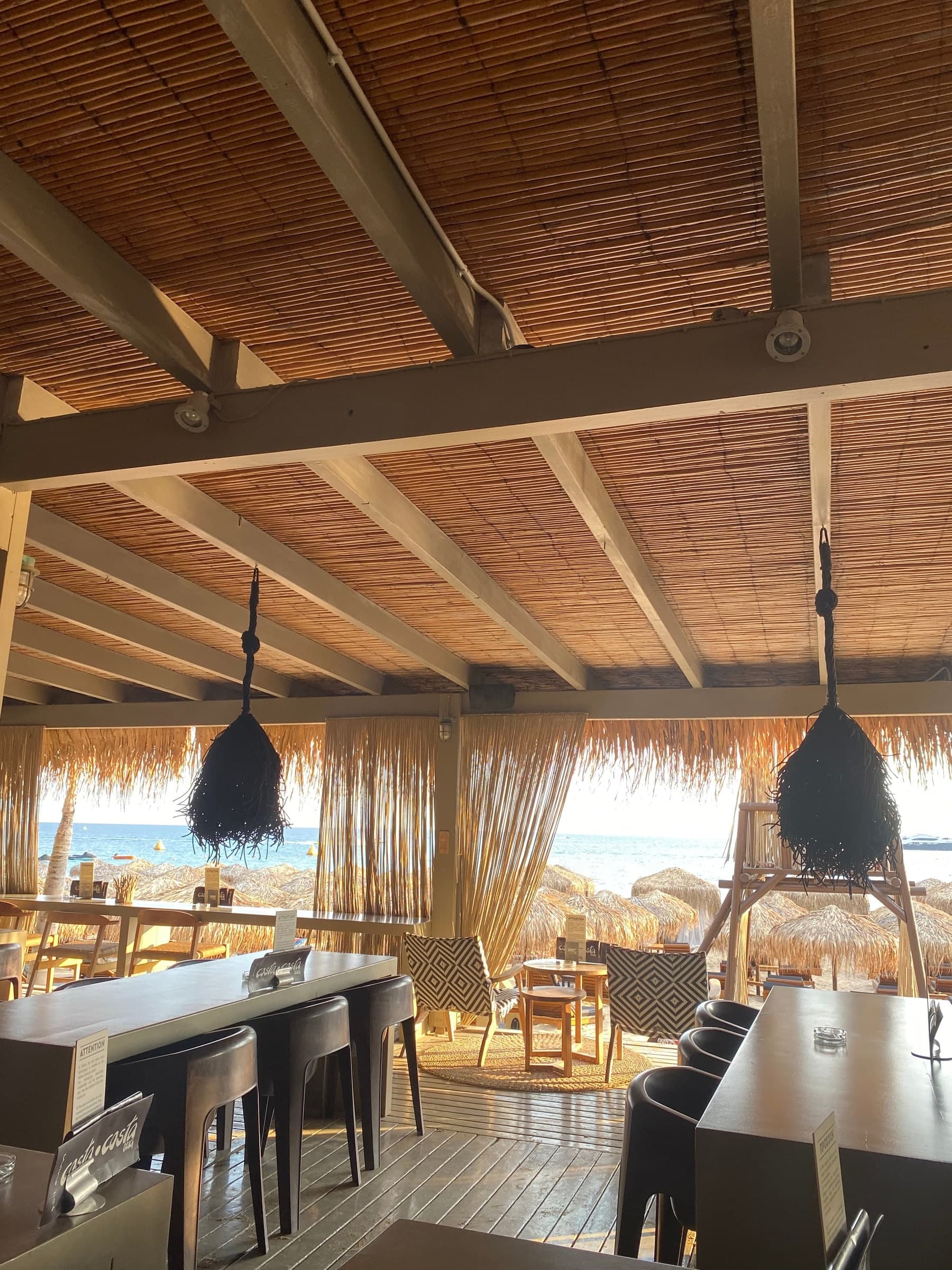 A beach restaurant under a reed roof, tables set, the sea beyond