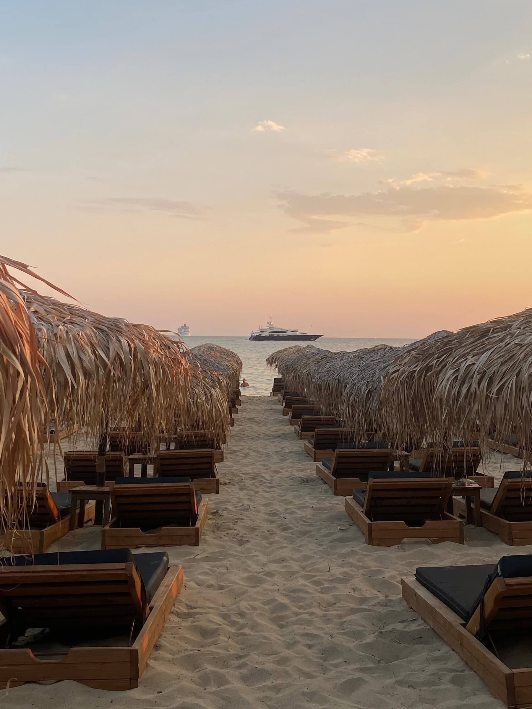 Two rows of straw umbrellas and sunbeds leading to the sea at sunset