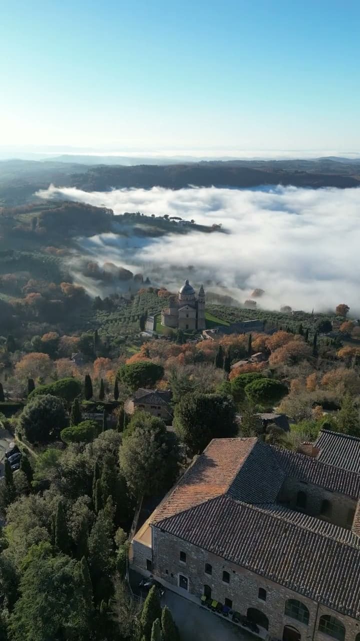 Drone footage over Tuscan trees and rooftops with a sea of fog behind