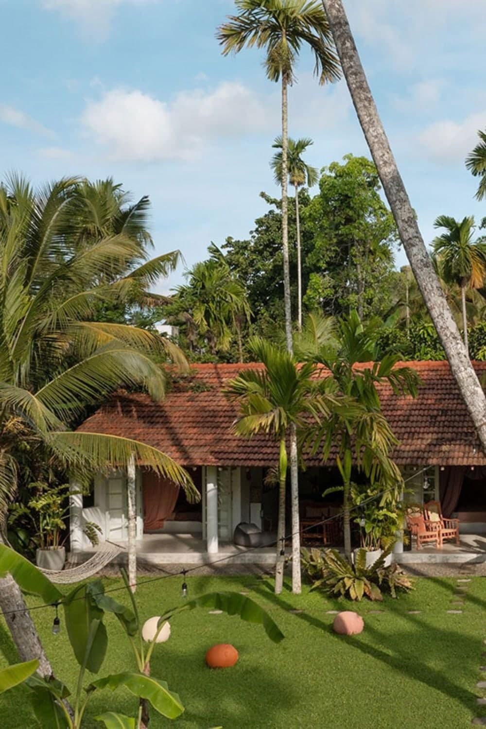 A villa with a red tiled roof in a tropical garden, palms and a hammock