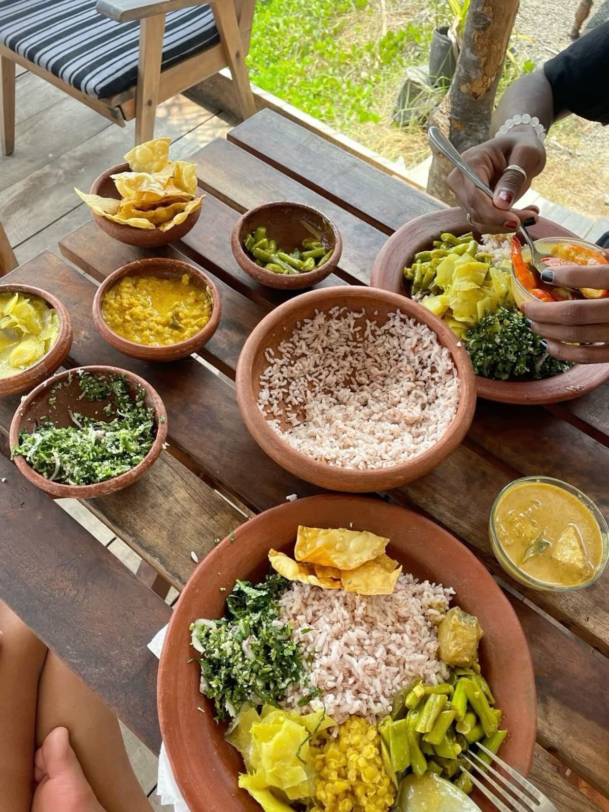 Rice and curry served in clay bowls on a wooden terrace table, from above