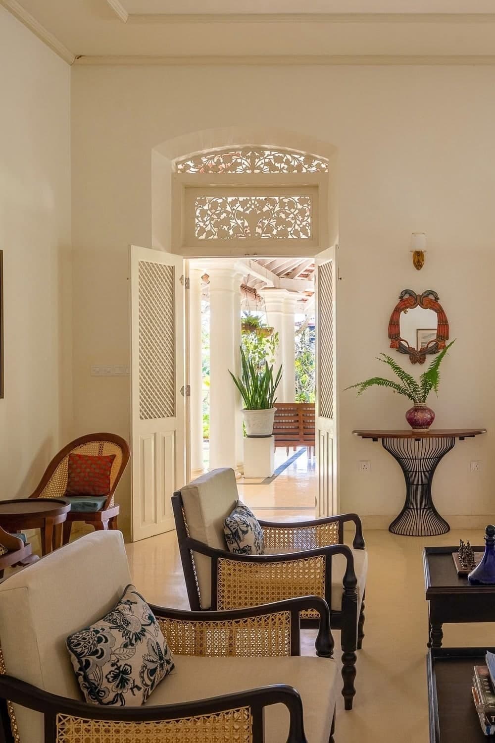 A colonial villa living room with rattan chairs and carved wooden doors open to the light